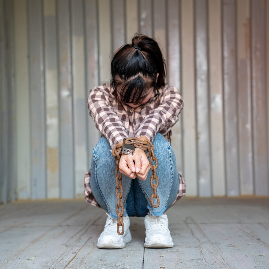 Woman with hands bound in chains sitting in empty shipping container